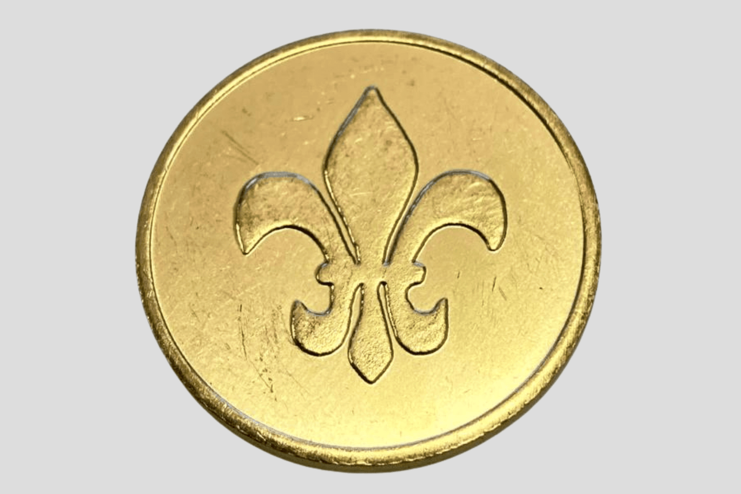 En gullmynt med fleur de lis på, som ligner Poletter metall preget På lager og produsert av JM Band®.