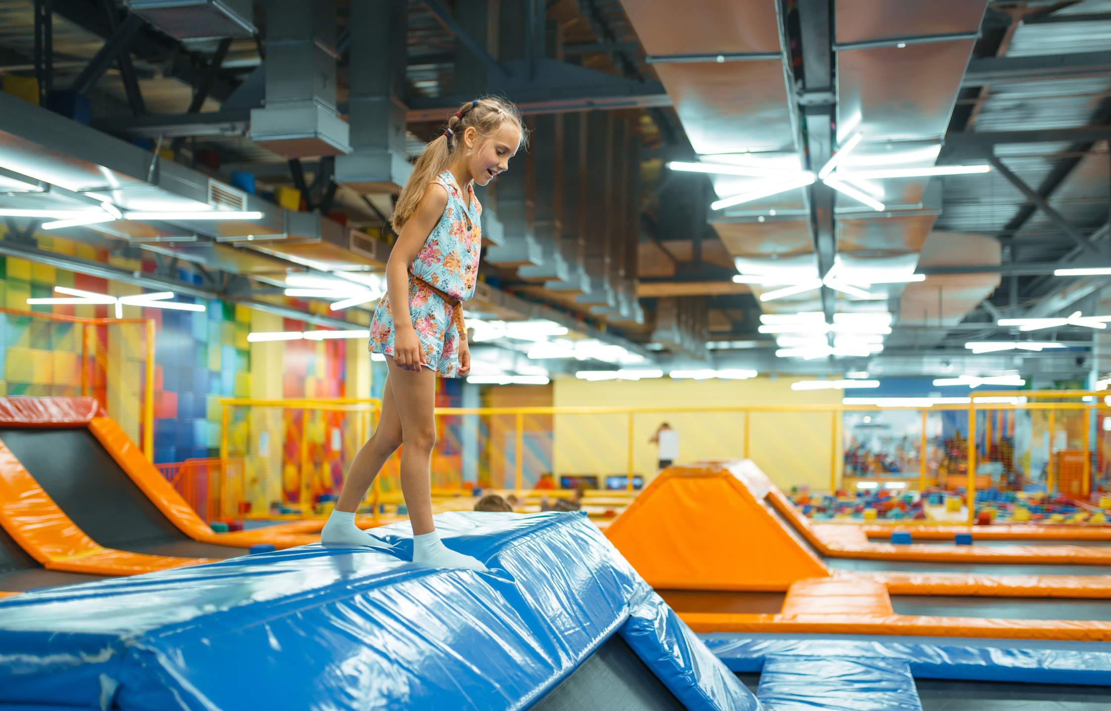 En jente som står på en trampoline på en innendørs lekeplass.